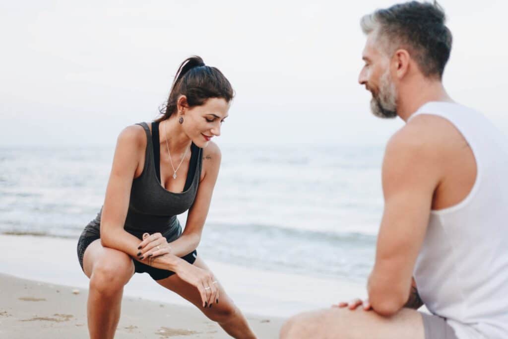 A man and woman on the beach doing stretching facing each other