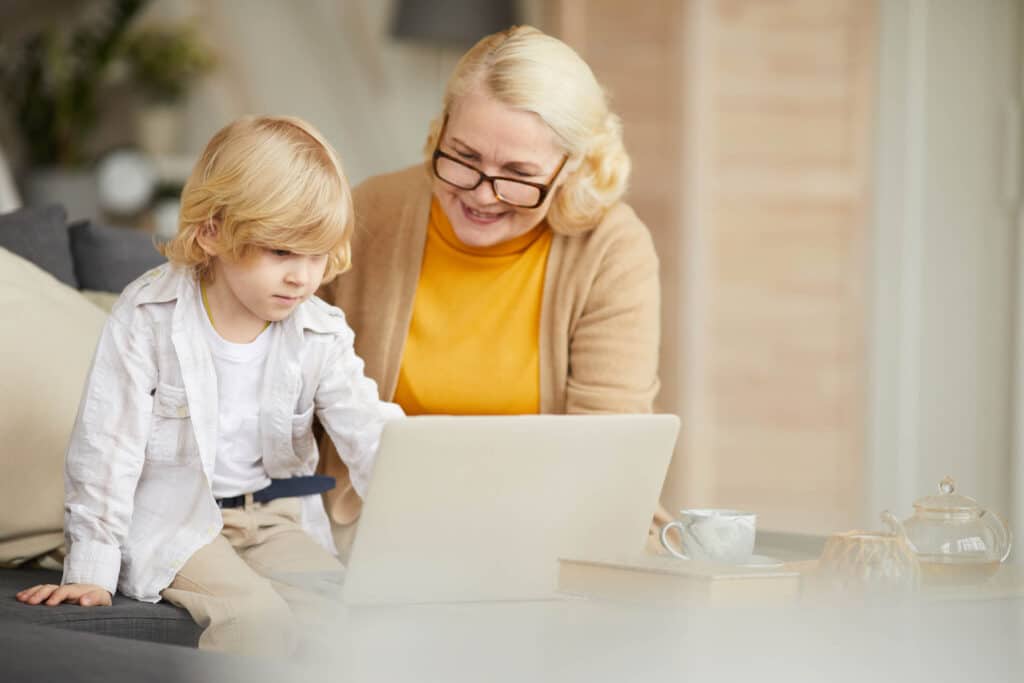 An elderly woman and a child looking in a laptop's screen while seated on a couch