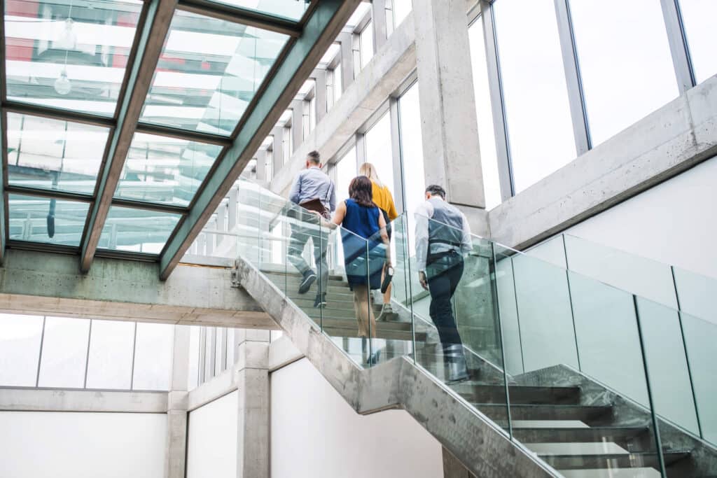 Four individuals ascending a high stairwell in a beautiful modern office building