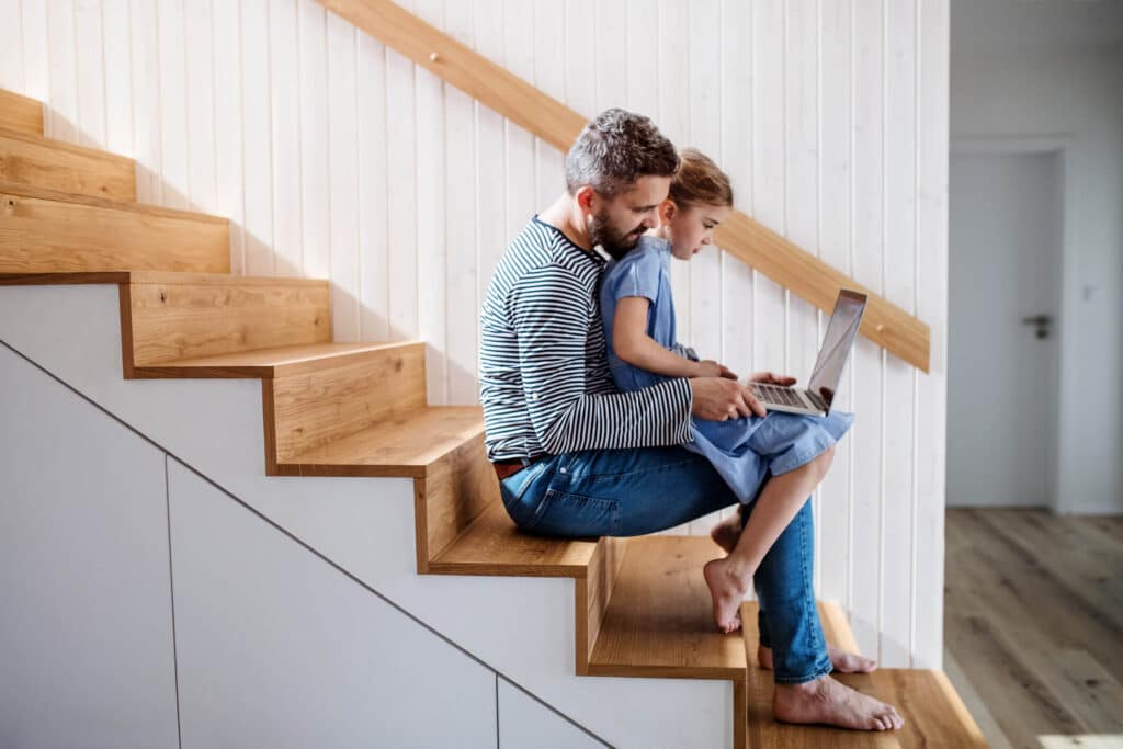 A father and daughter using a laptop together while sitting on the staircase