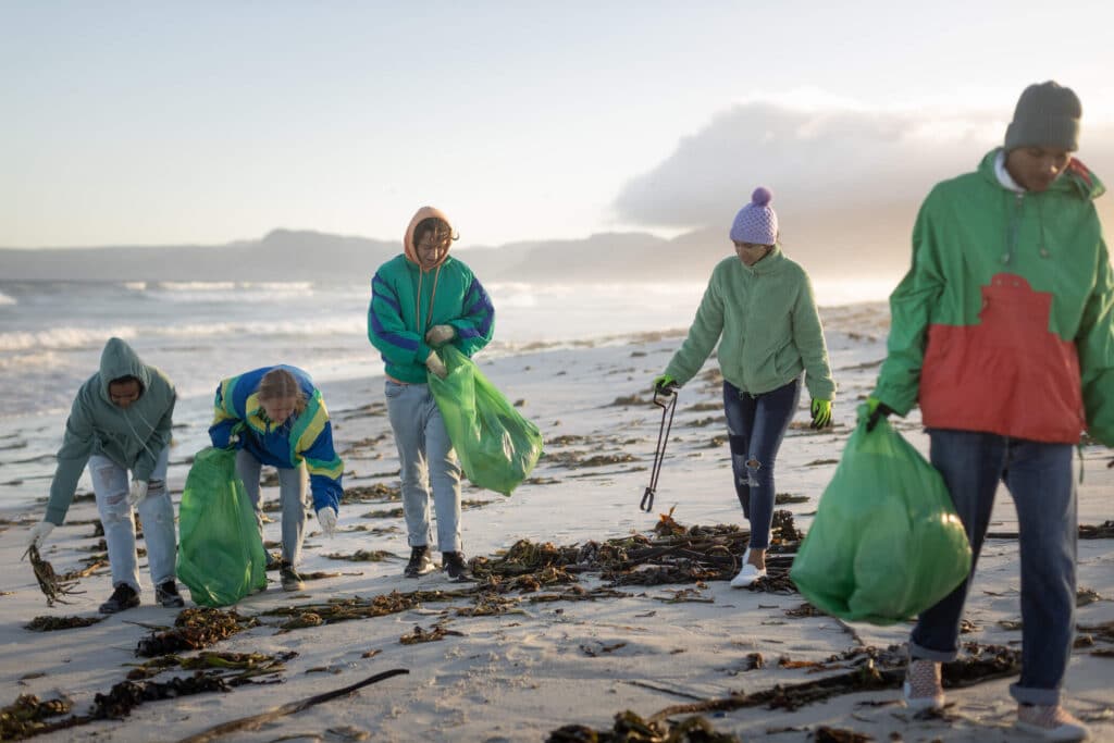 A group of individuals carrying green trash bags while doing a beach clean up drive