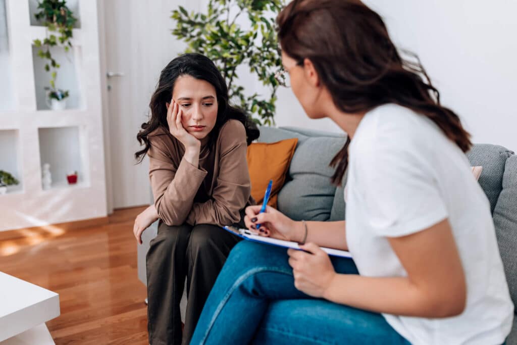Two woman sitting on a couch engaged in conversation during an in person therapy consultation