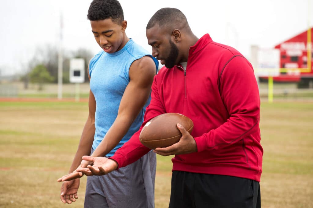 A father and son standing in the middle of a football field grasping a football while looking at their hands