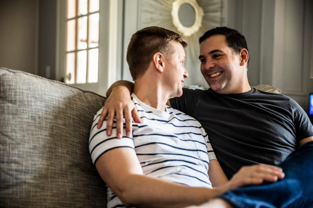 Two men enjoying each other's company while sitting on a couch, sharing smiles and laughter.
