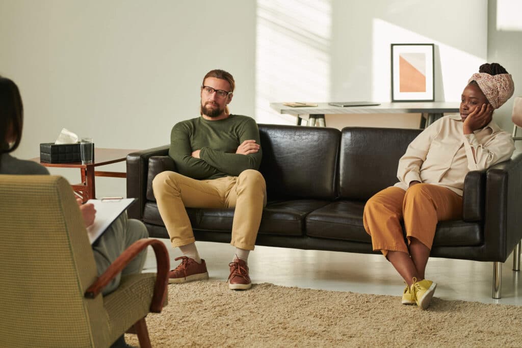 A man and a woman sitting on the both end of the couch and engaged in a conversation while having an in person visit with a therapist
