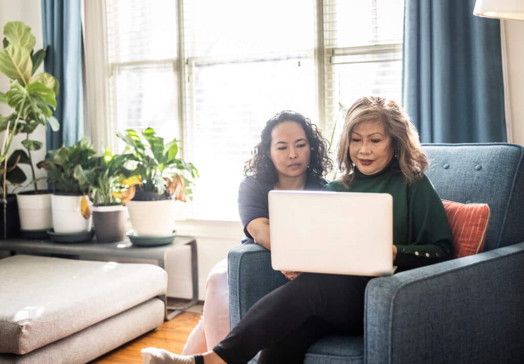 Two women sitting on a couch while working on a laptop computer