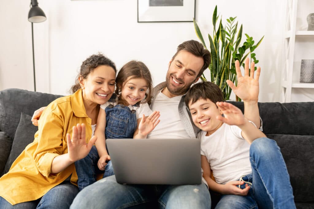 A happy family gathered on a couch waving at their therapist through a video call