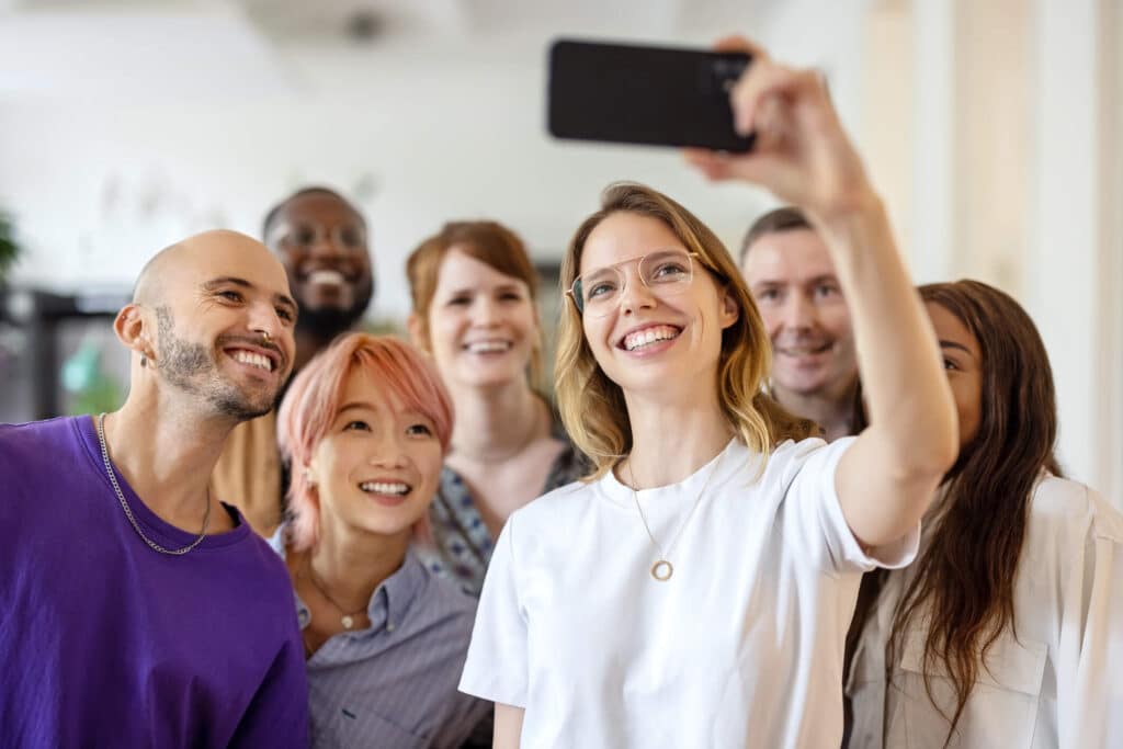 A group of individuals smiling and posing together while capturing a self-portrait using a mobile device