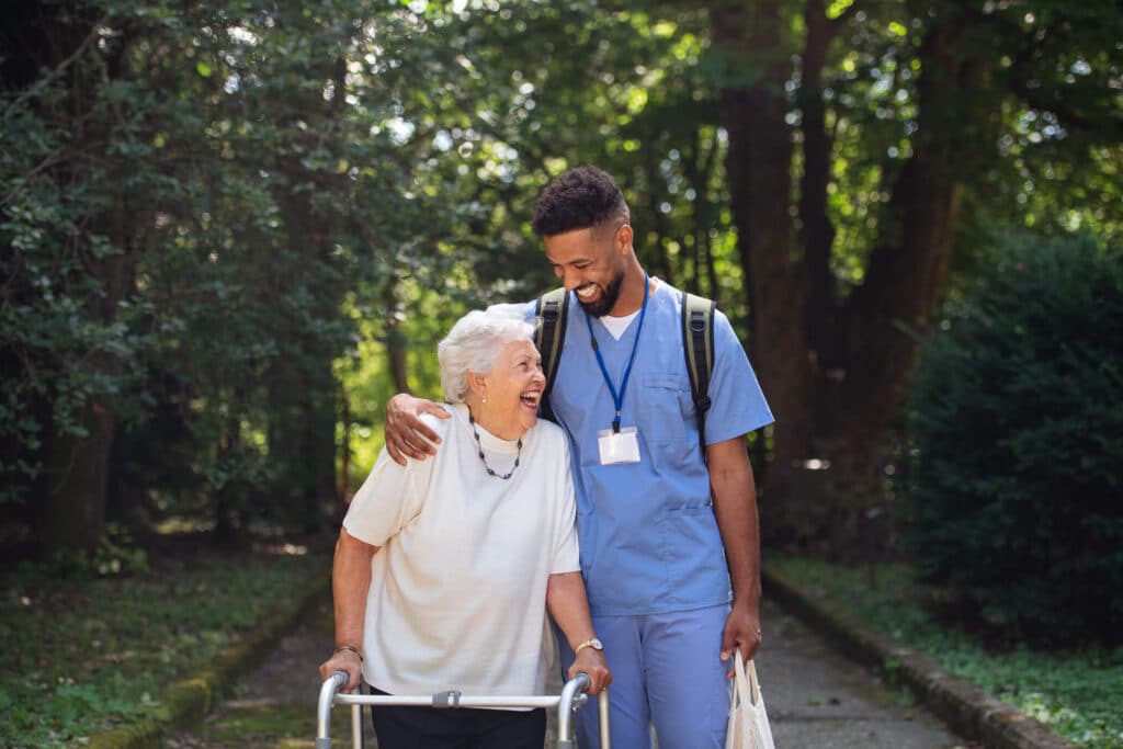 A smiling nurse holding and assisting a happy senior woman walk