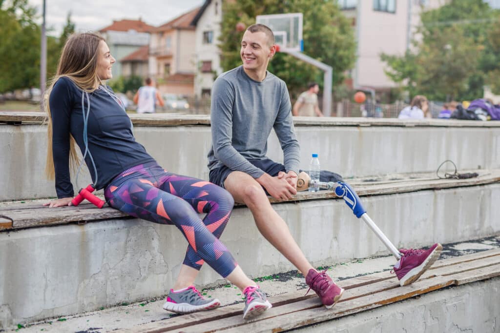 An amputee man and a woman taking break from exercising and sitting on a bench