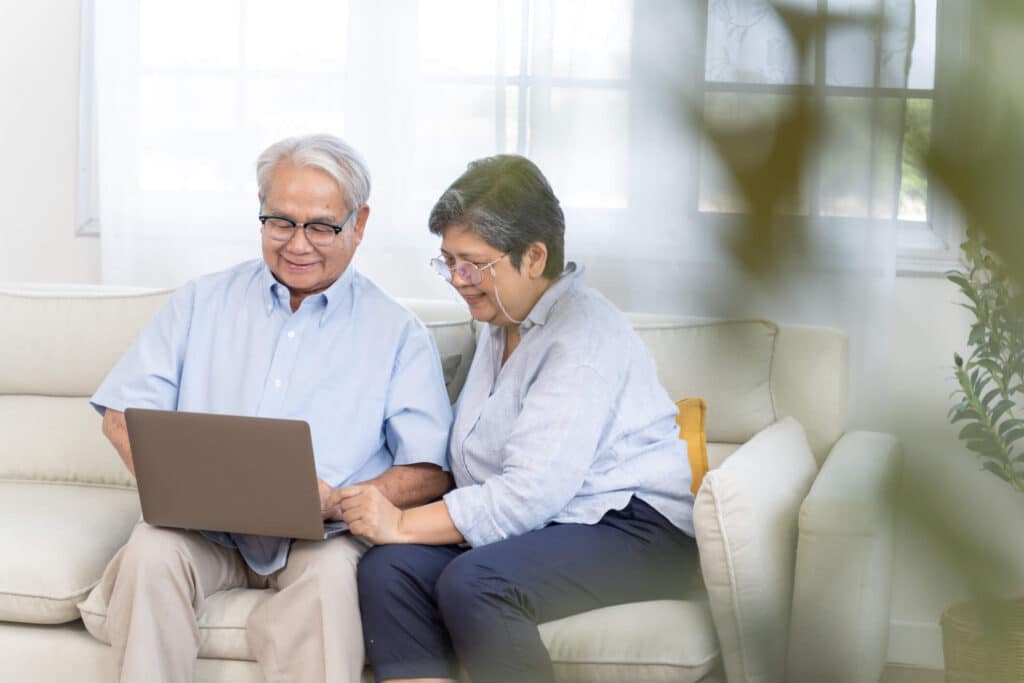 Senior couple smiling in front of a laptop while seated on a white sofa
