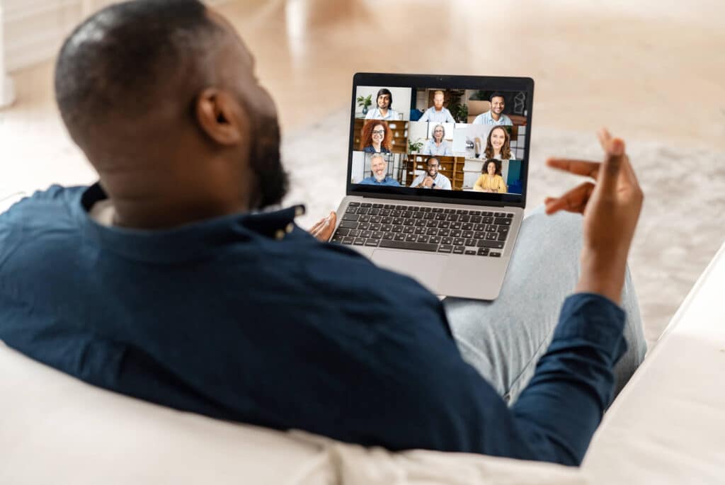 A man sitting on a couch with a laptop on his lap and having a virtual group meeting