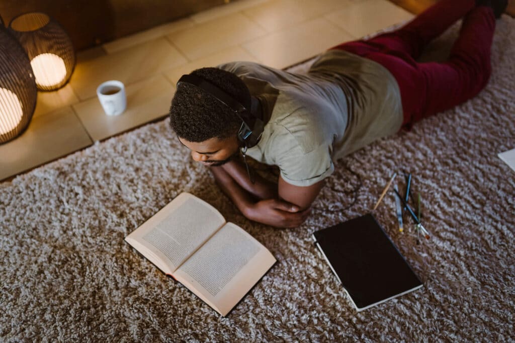 A man lying on the floor wearing headphones while reading a book