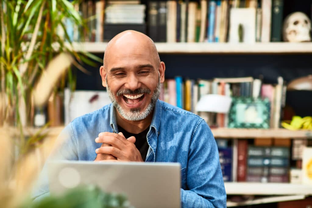 A man with no hair wearing a smile, engrossed in his work on a laptop showing happiness and contentment