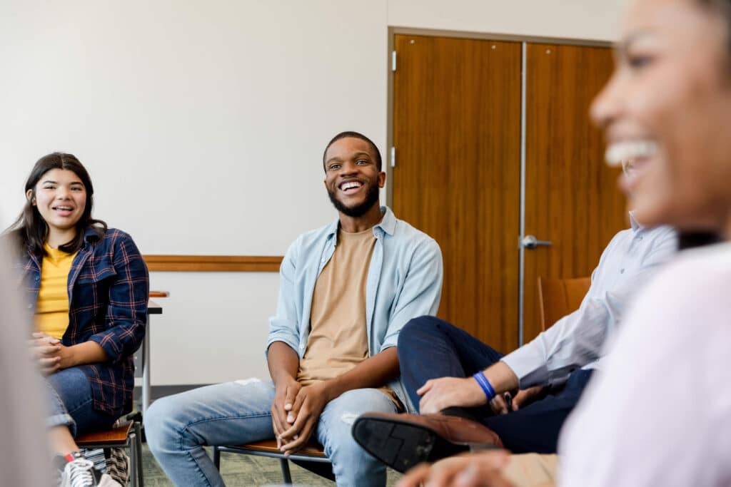 A diverse group of individuals sitting in a circle with smile on their faces during a group therapy session