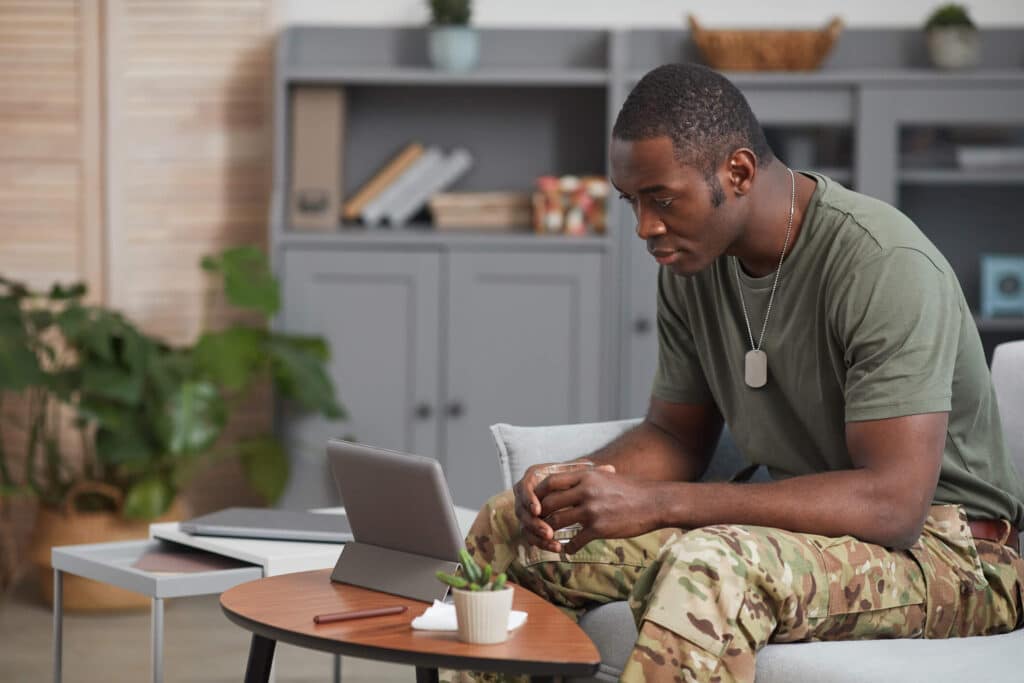 A male military officer seated on a sofa looking at his ipad on the table