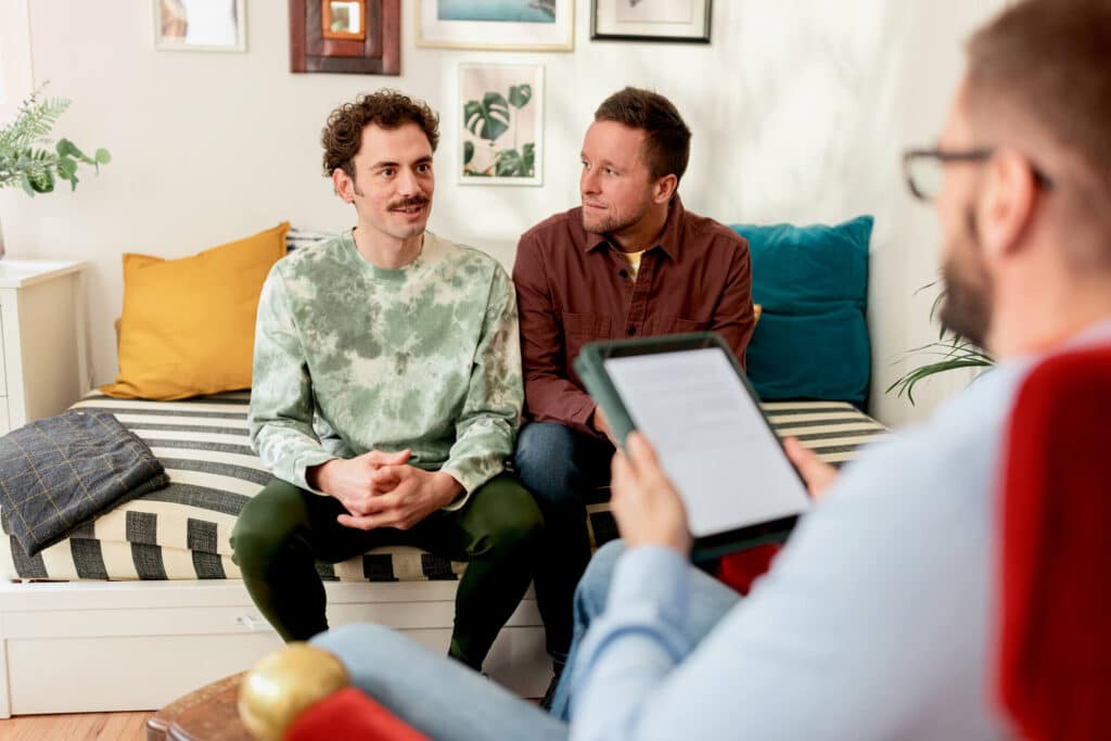 Two men sitting on a couch while having an in person consulation with a therapist