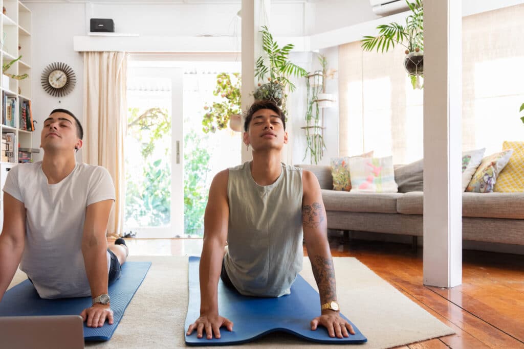 Two men gracefully performing yoga poses on top of blue mats in a serene living room