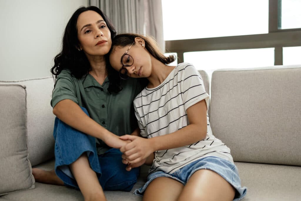 A sad mom and daughter comforting each other while seated on a couch