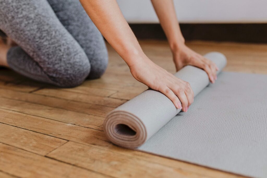A woman kneeling on the floor while rolling up a yoga mat