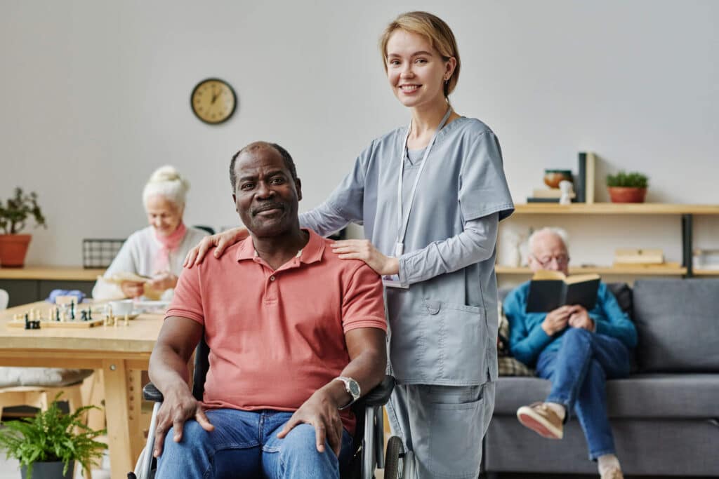 A smiling nurse attentively assists an elderly man seated in a wheelchair providing compassionate support and therapeutic care