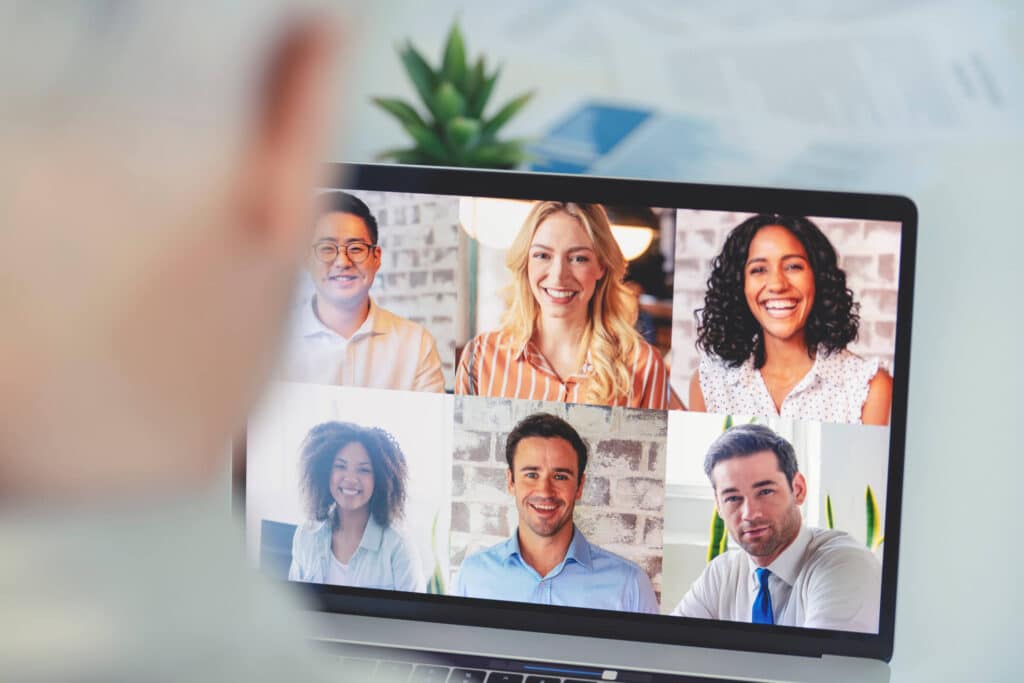 A laptop screen displaying an online meeting with a group of smiling individuals engaged in a discussion