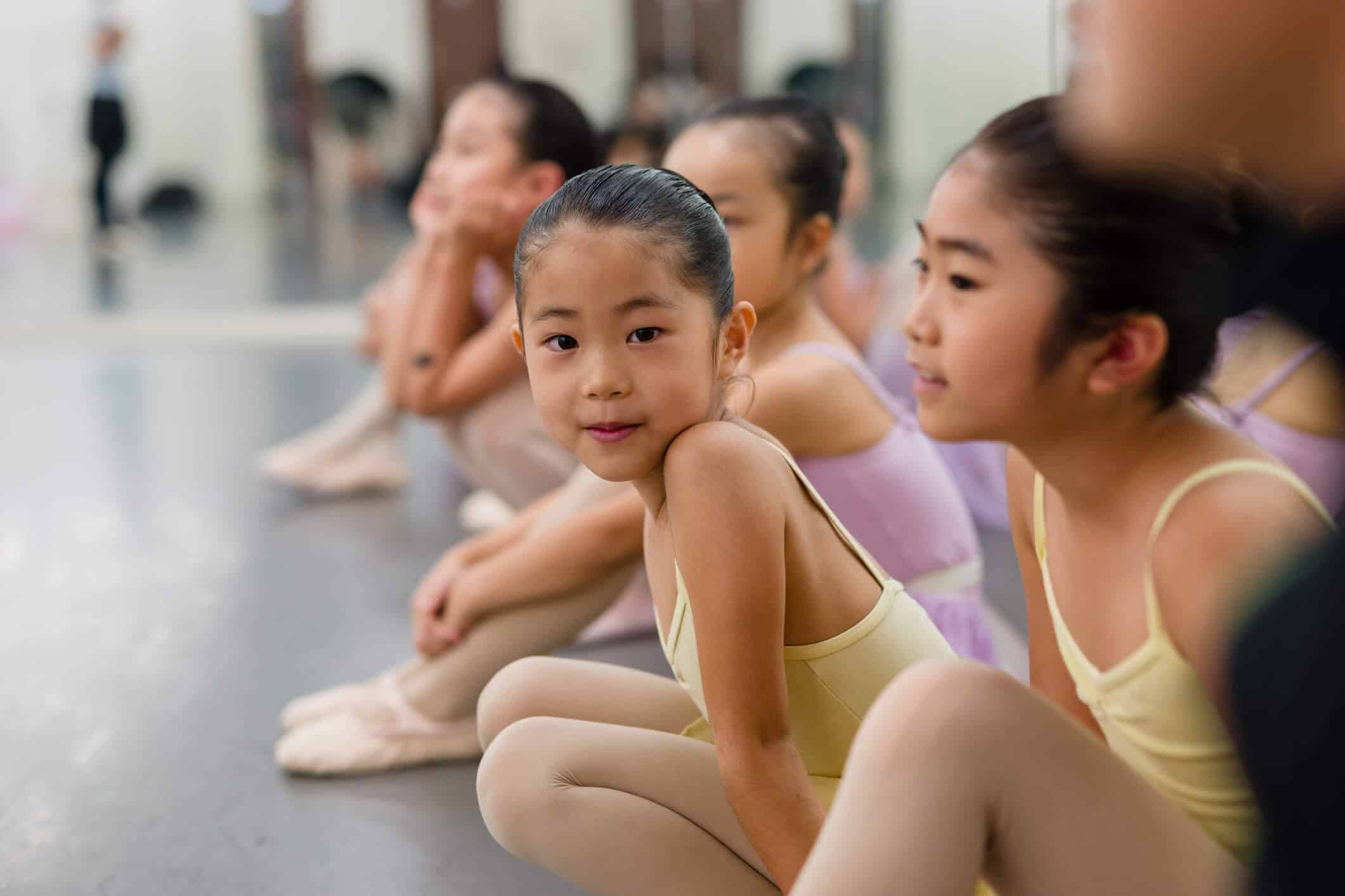 A group of young girls wearing yellow and purple ballerina dresses sitting happily on the floor
