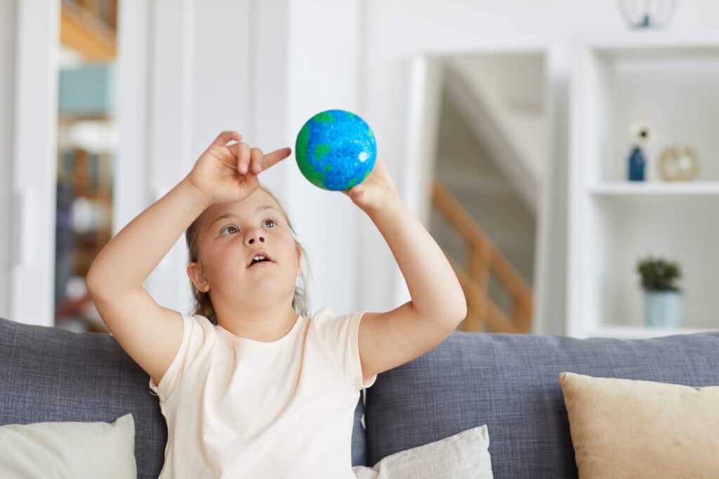 A little girl sitting on a couch while pointing her finger to the globe she is holding