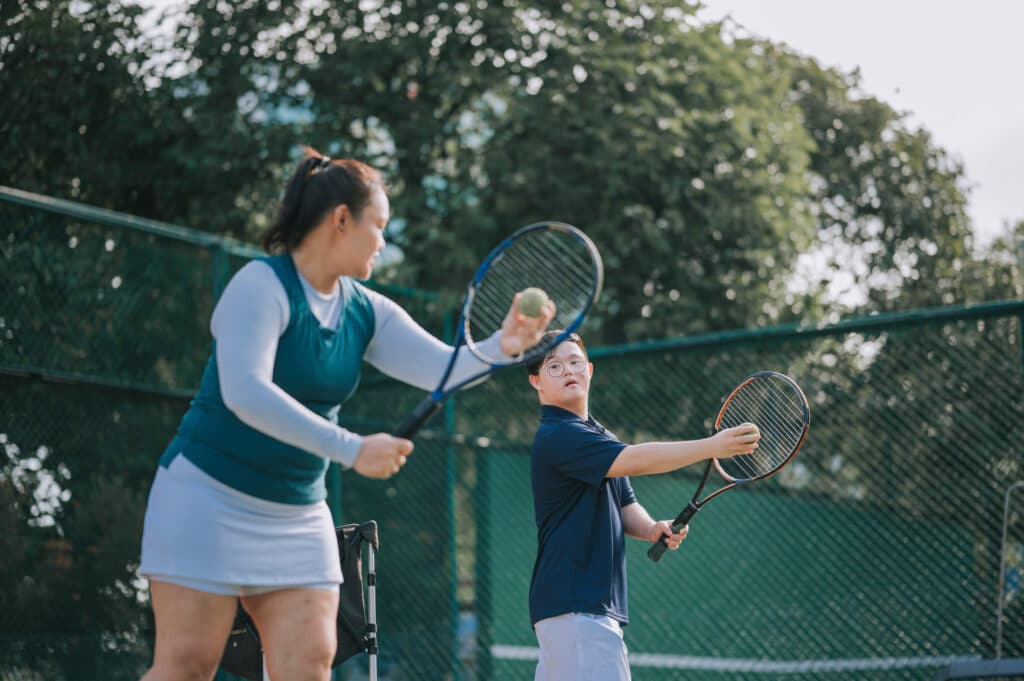 A girl showcasing her skills and teaching the boy with eye glasses how to play tennis on a court