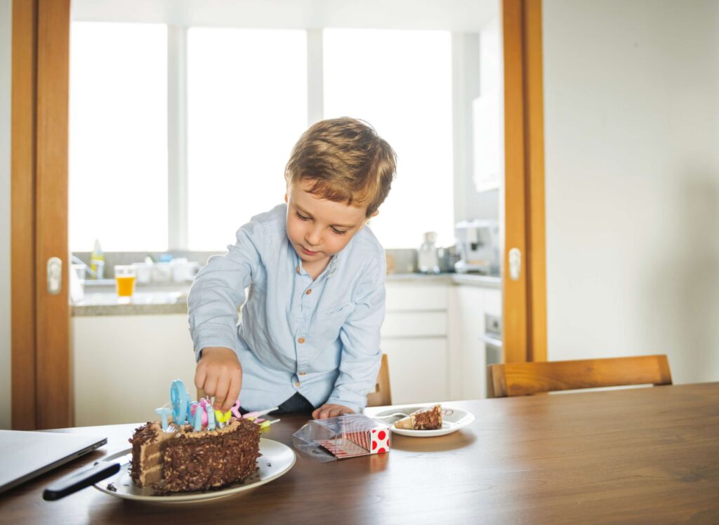 A cute little boy standing on a kitchen chair while fixing the candles on the cake
