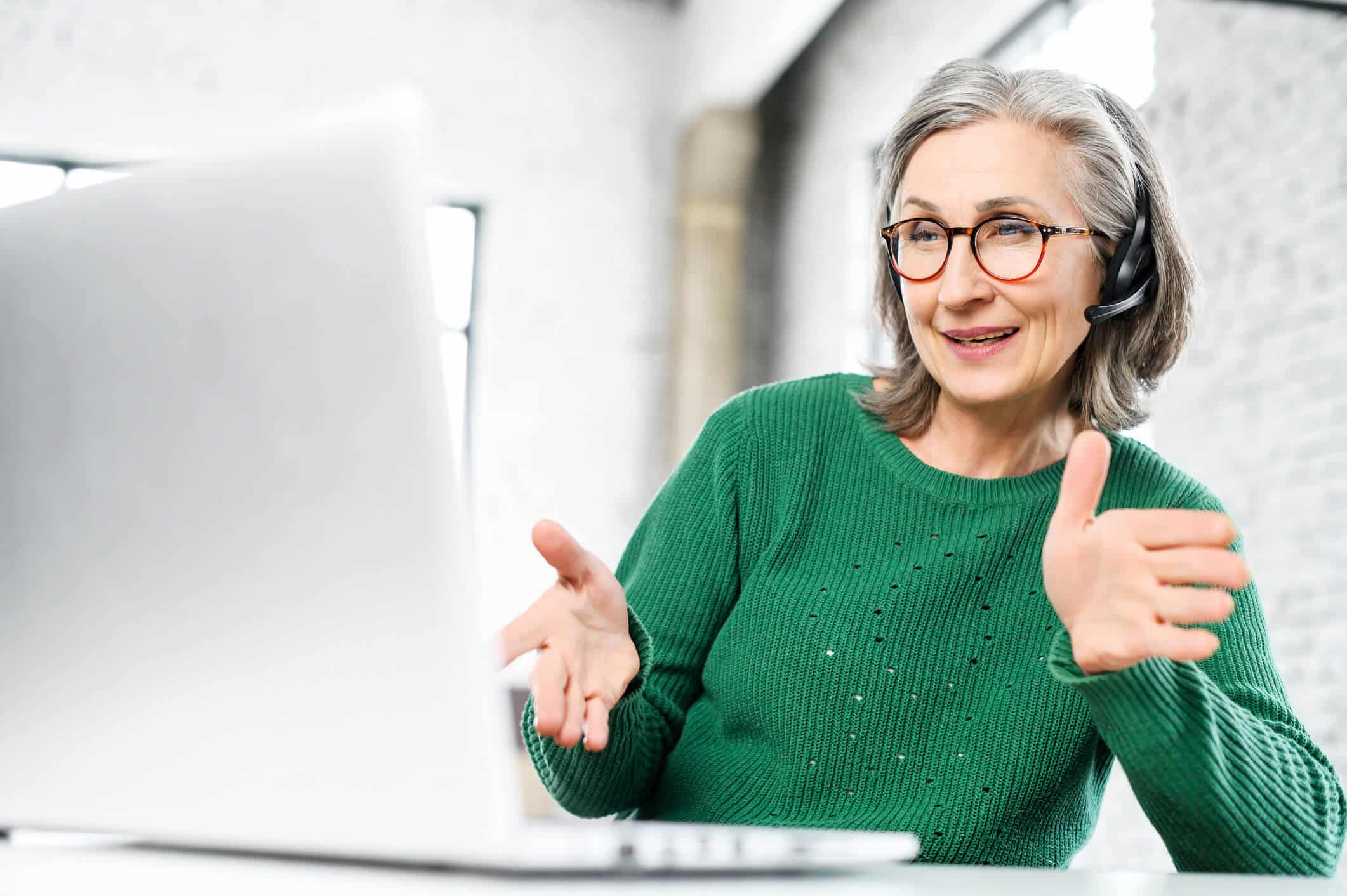 An elderly woman wearing glasses and green sweater while having an online consultation