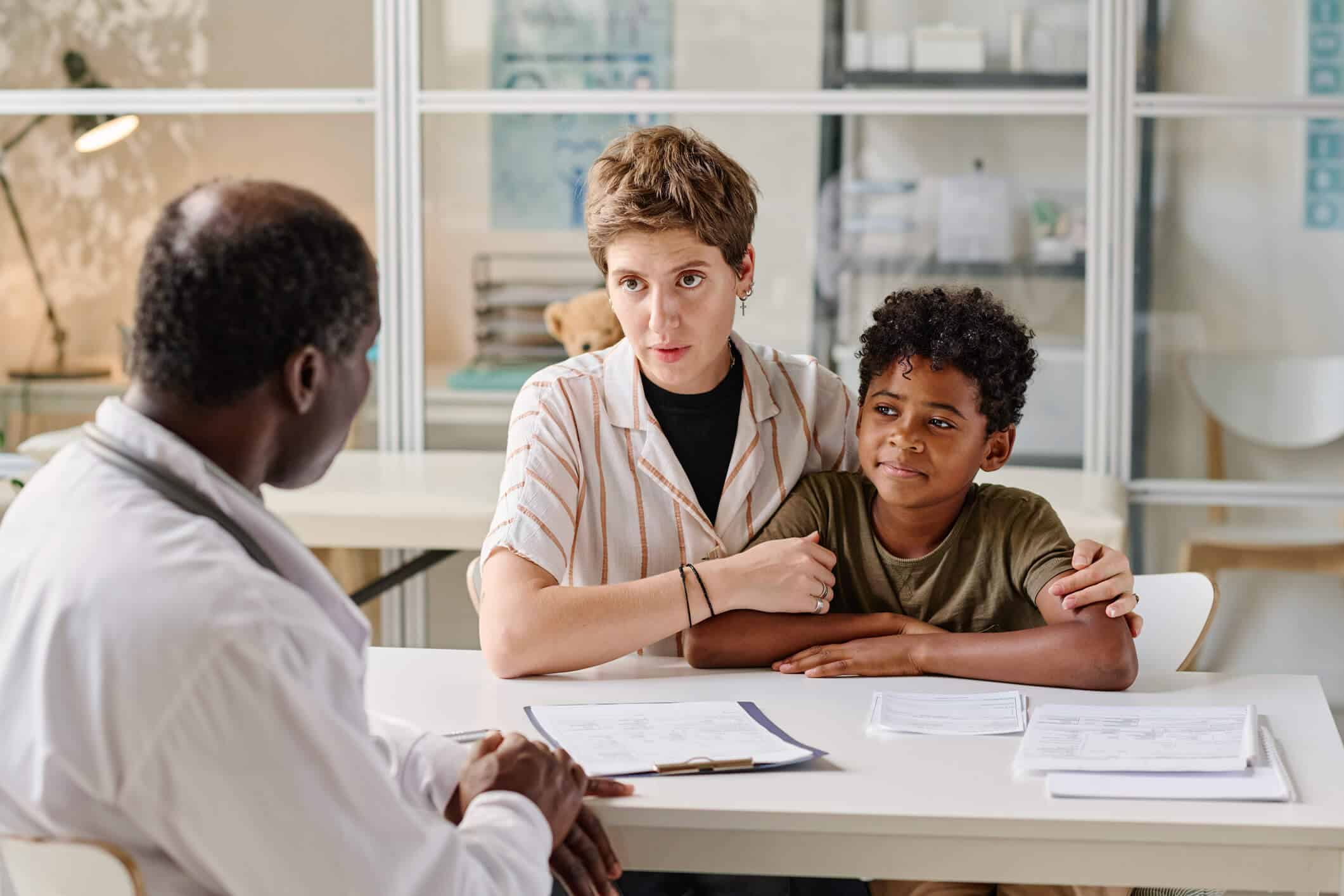 A woman and a young kid sits at a table in front of a therapist during an in person visit