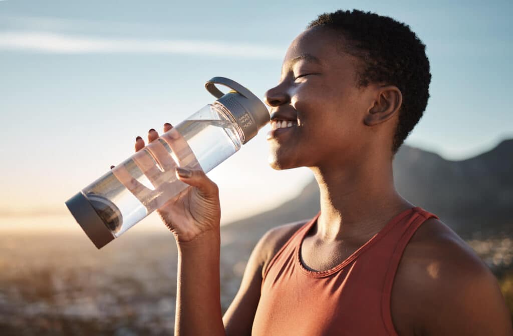 A woman holding a water bottle in the middle of nowhere while the sun is shining on her face