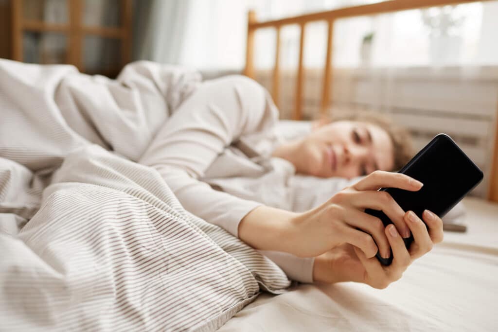 A woman lying in a comfy looking bed while broswing through her phone