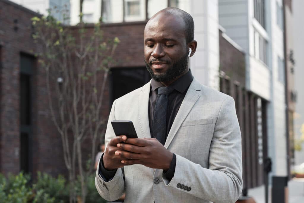 A man wearing a gray suit standing outside an office building while scrolling through his phone