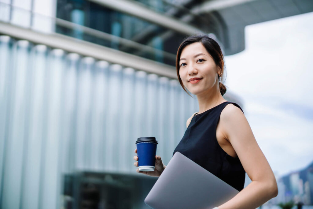 A woman wearing a black top holding a laptop and a coffee mug